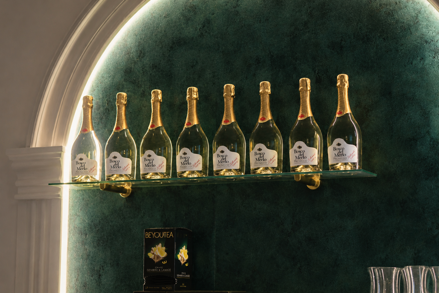 Un rând de sticle de Prosecco iluminate într-o firidă verde-smarald la bar